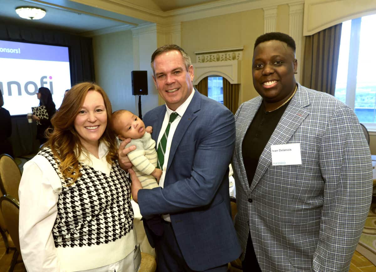 Rep. John Lawn, holding a baby, smiling for the photographer, along with the baby's parents, the Delanois Family.