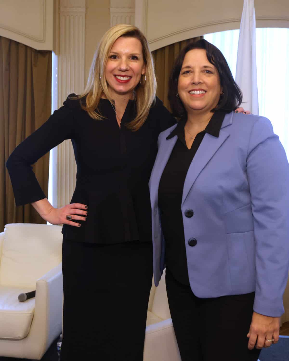 MassBio CEO and President Kendalle Burlin O'Connell in a black dress posting for a photo with Massachusetts Lt. Governor Kim Driscoll who is wearing a lavender jacket.
