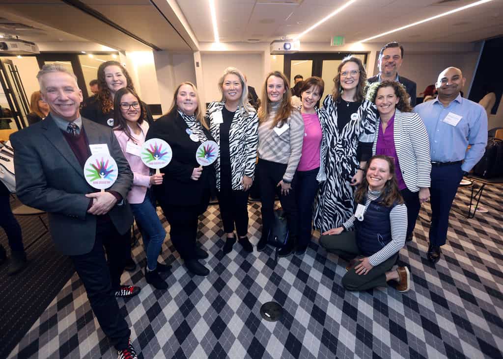 A group of 12 men and women, many in zebra patterned or black-and-white striped clothing, smiling for the photographer and holding Rare Disease Day hand signs.