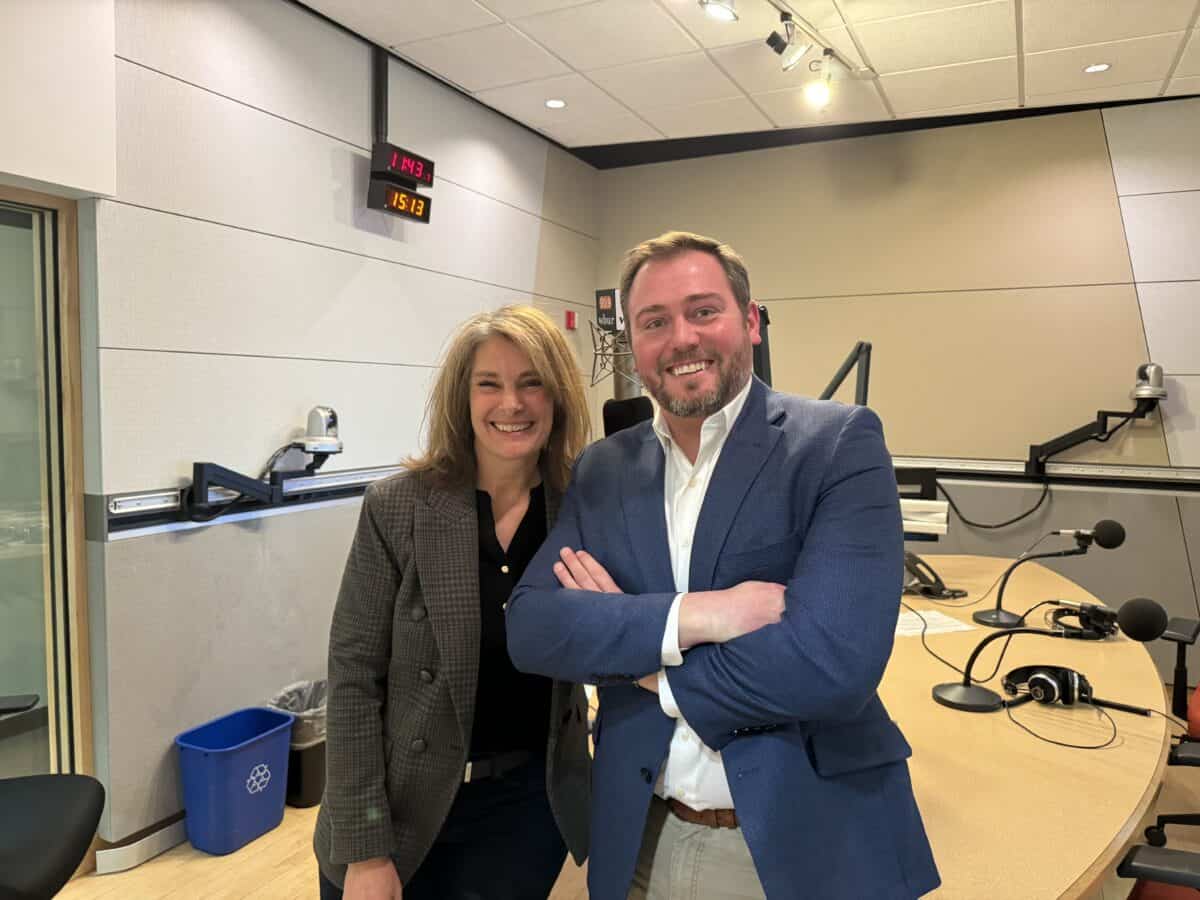 MassBio's head of external affairs, Ben Bradford, wearing a blue blazer and open collar shirt, poses for a photo in the radio broadcast studio of WBUR with Tiziana Dearing, who is wearing a plaid blazer, following a live interview on lab development.