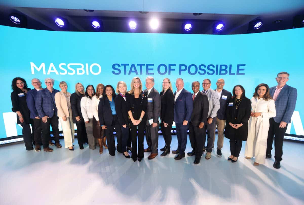 MassBio Board Members and CEO & President Kendalle Burlin O'Connell pose in front of a large video screen with the MassBio logo and the words State of Possible.