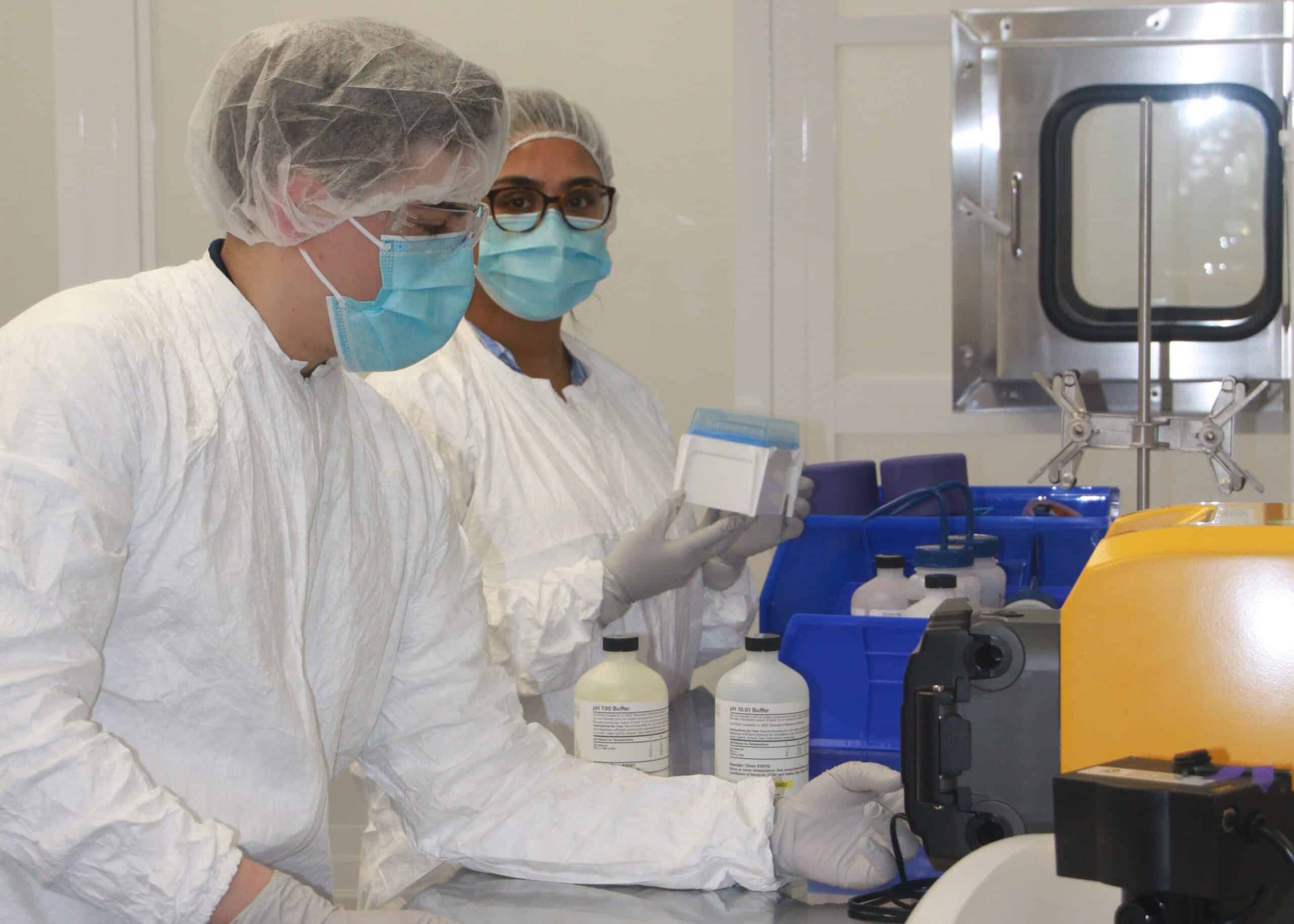 Lab technicians with hair nets and face coverings operating lab equipment.