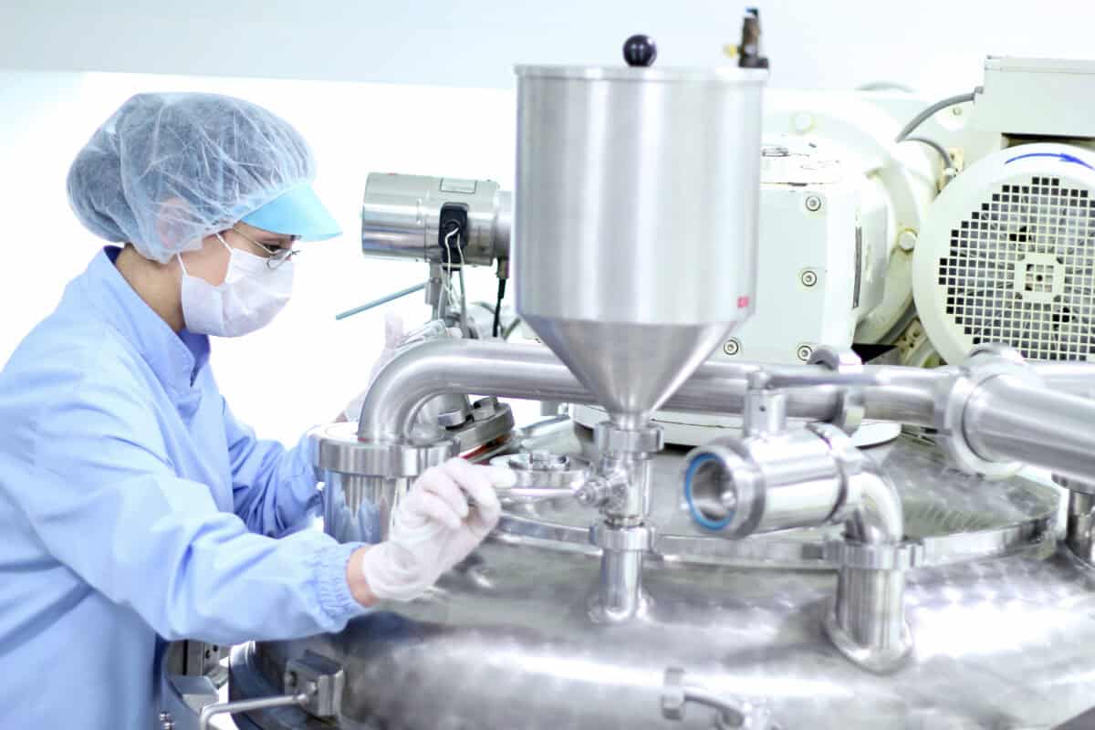 A female lab technician in gloves, mask, and a hairnet preparing a machine for work in pharmaceutical factory.